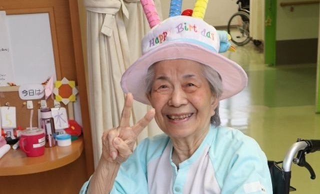 ハッピーバスデーの帽子をかぶりピースする高齢の女性